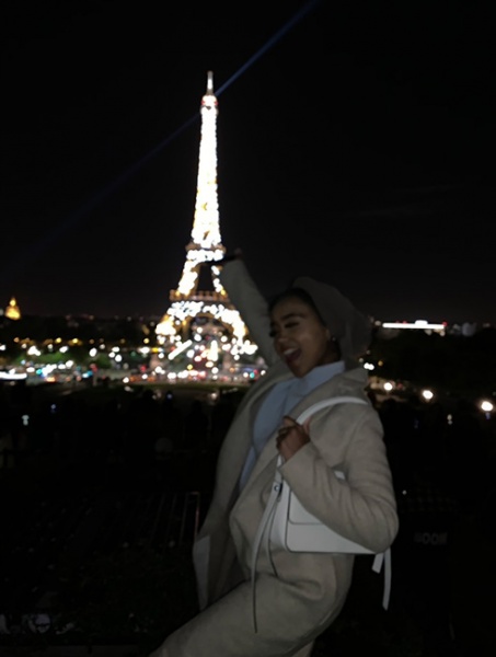 Aisha Burka poses in front of the lit up Eiffel Tower