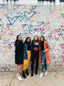 Melanie and friends posing in front of artistic backdrop.