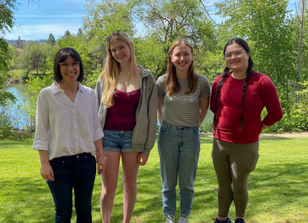 Four people (the Geck lab members) standing outside on a grassy college campus lawn on a sunny day
